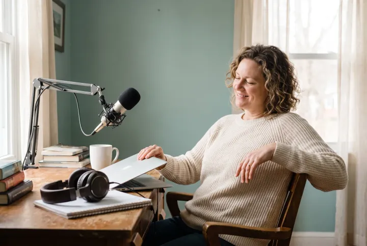 Podcast host closing her laptop after signing up, microphone and headphones on her home studio desk